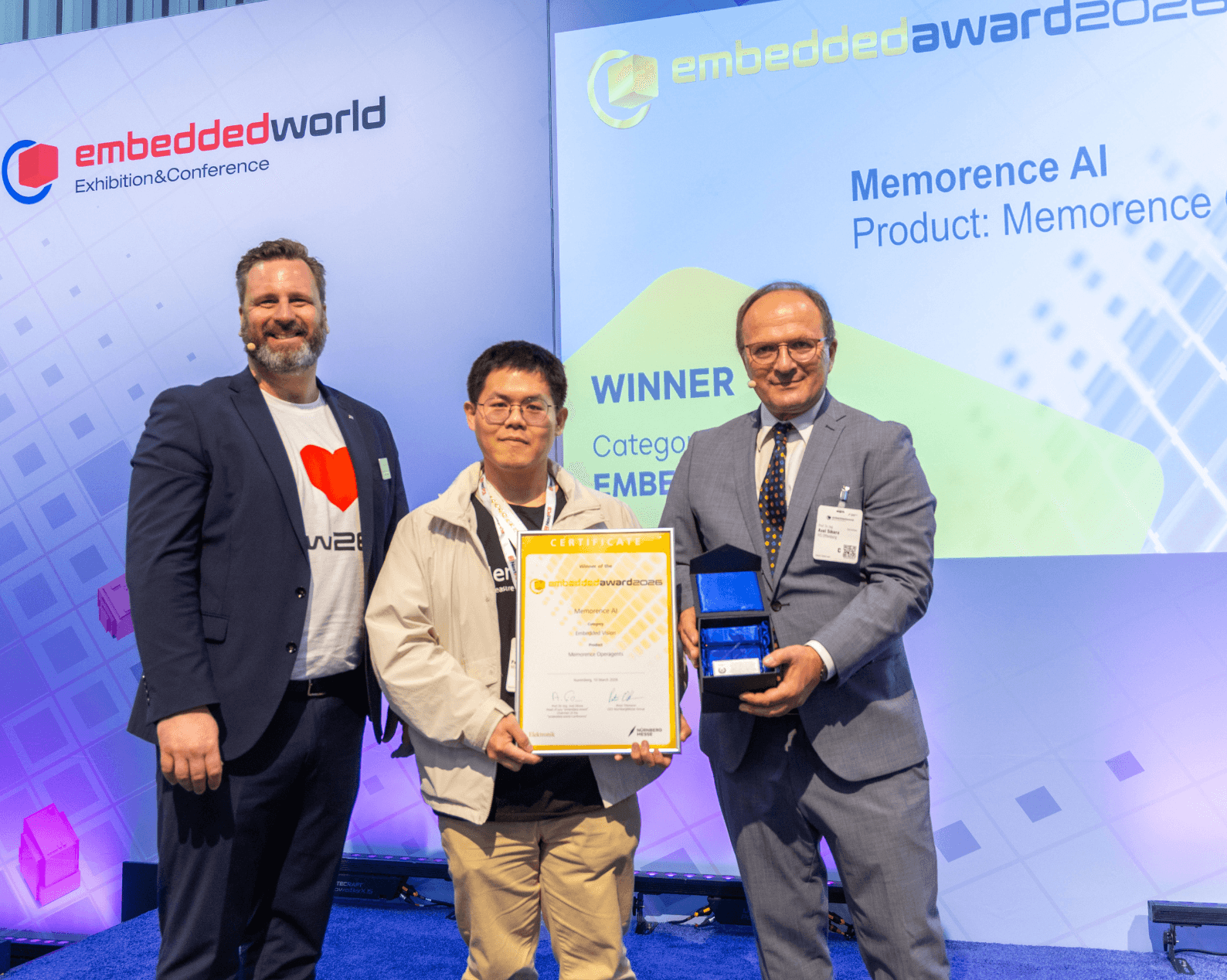 Drei Männer in Businesskleidung mit Zertifikat und Glastrophäe auf der Award Bühne.