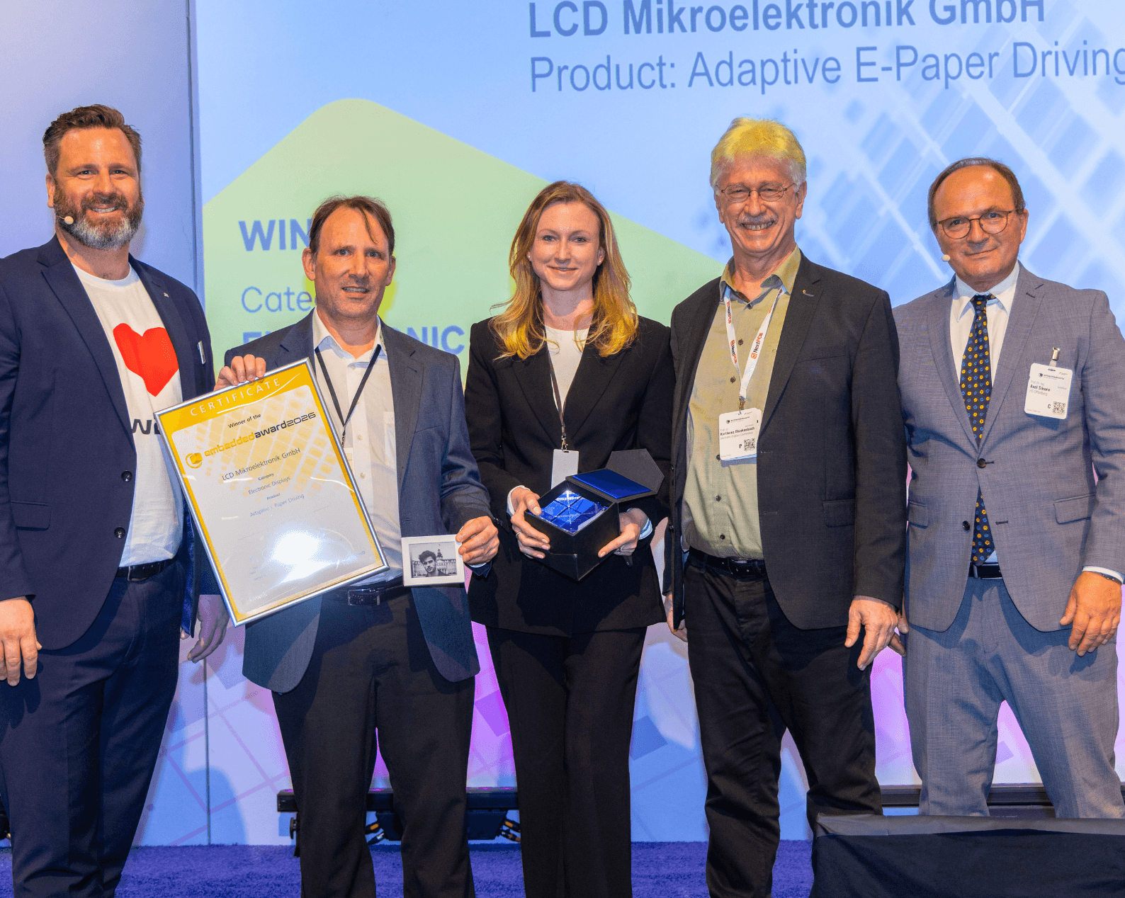 Vier Männer und eine Frau in Businesskleidung mit Zertifikat und Glastrophäe auf der Award Bühne.