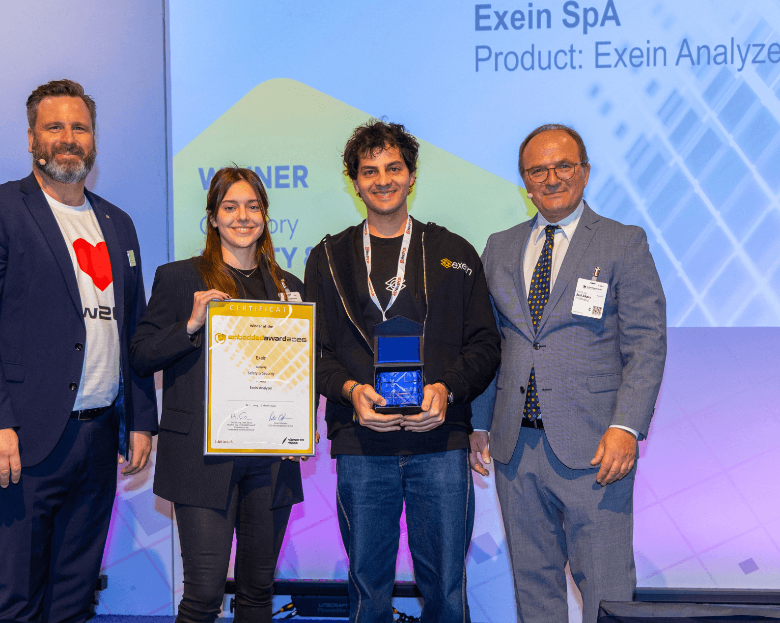 Drei Männer und eine Frau in Businesskleidung mit Zertifikat und Glastrophäe auf der Award Bühne.