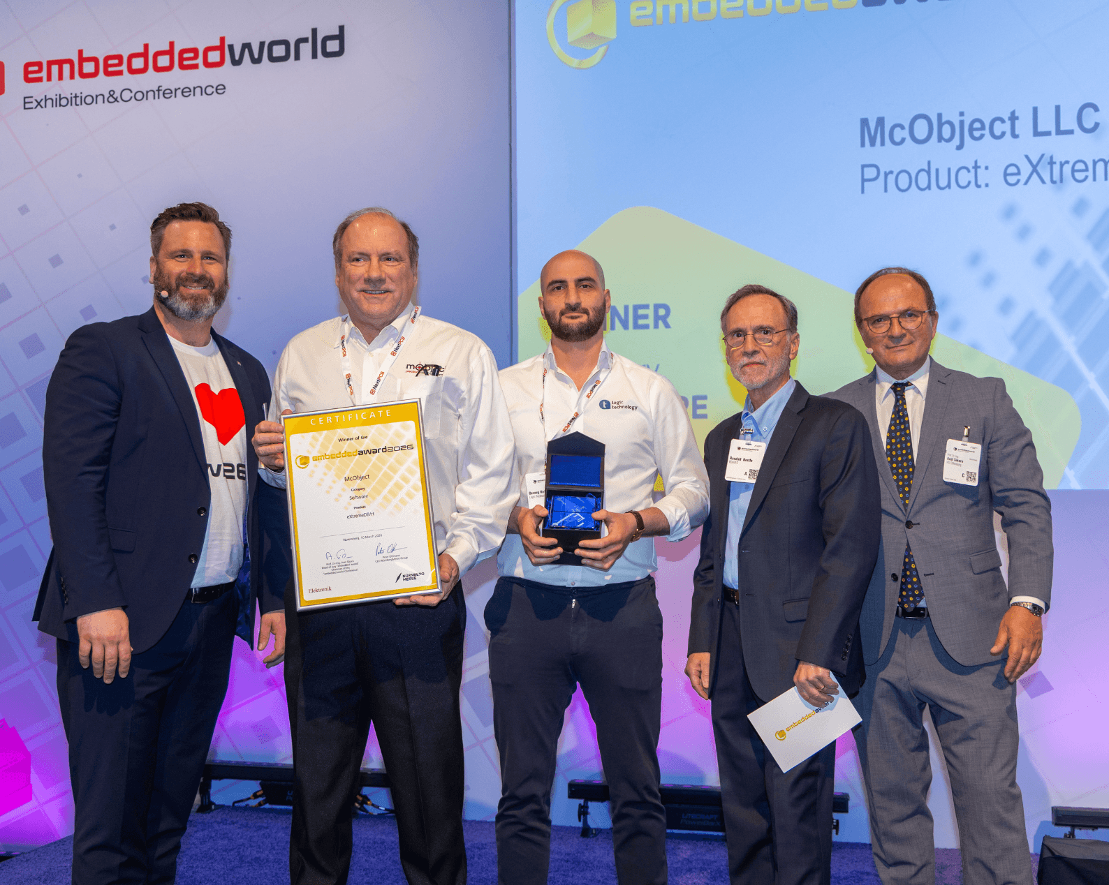 Fünf Männer in Businesskleidung mit Zertifikat und Glastrophäe auf der Award Bühne.