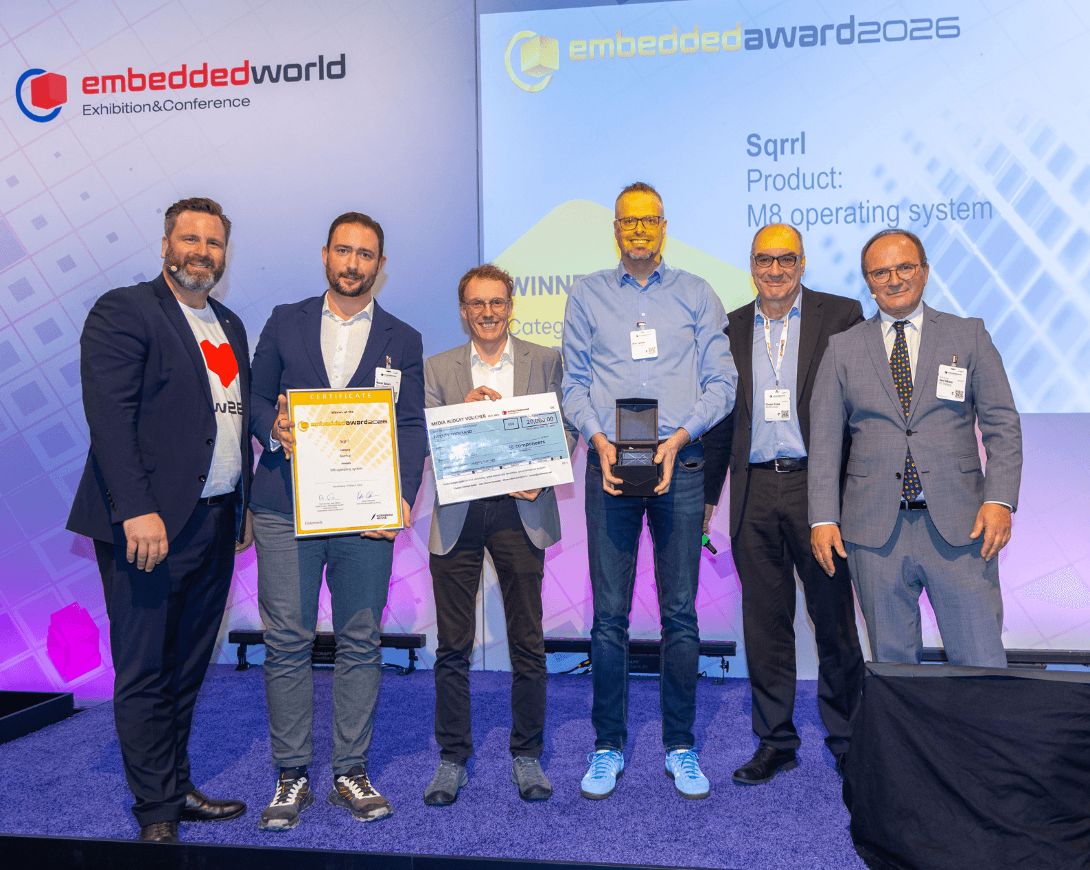 Sechs Männer in Businesskleidung mit Zertifikat und Glastrophäe auf der Award Bühne.