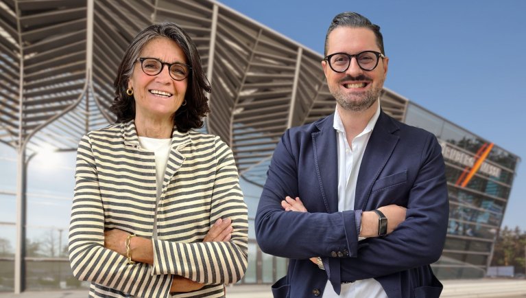 Two people in front of a modern building with folded arms.
