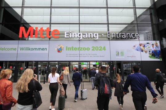 Menschen strömen zu einer Halle der NürnbergMesse mit Aufschrift „Willkommen / Welcome Interzoo 2024“.